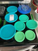 Photo of assorted Anchor Hocking glass storage containers with various blue and green plastic lids on a black stove top.