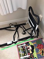 Full view of the black and white bed rail with attached straps on carpet near a wall and rug.