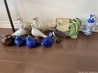 Front view of all ceramic birds and figurines including white birds, blue birds, brown bird, green fish vases, and blue and white fish figurine.