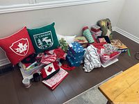 Photo showing Canada Day and Christmas-themed decorations arranged on floor including cushions, mugs, napkins, flags, gift boxes, and throws.