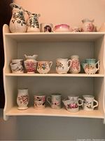 Shelf displaying assortment of porcelain vases, shaving mugs, and a pitcher with floral decorations