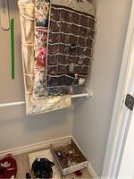 Three hanging jewelry organizers in fabric with clear pockets filled with mixed costume jewelry items such as earrings, necklaces, watches, and key chains placed on a closet rod and in a box below.