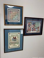 Photo showing all three framed needlepoint and cross stitch artworks on the wall.