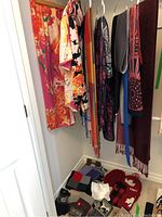 Overview of scarves hanging on hangers and mitts, gloves, and toques on the floor
