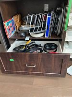 Overall view of shelf with stacked baking sheets, muffin tin, bundt pan, cutting boards, trays, and visible pans in an open drawer below.