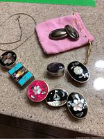 Overview of all pillboxes, earrings and chain shown on countertop with pink pouch