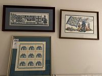 Three framed textile artworks on wall showing needlepoint and cross stitch patterns and scenes