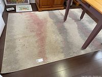 Full view of the rectangular area rug on a hardwood floor beneath a wooden table, showing the faded rose and gray gradient pattern and signs of wear.