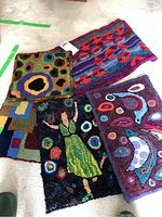 Five finished colorful rug hooking patterns laid side by side on carpeted floor, showing distinct colors and designs