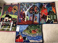 Four colorful finished rug hooking patterns laid out side by side showing diverse bright designs mainly of houses and trees