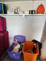 Two plastic storage totes, purple and orange, shown with hand-hooked bunny pillow and Halloween doll inside.