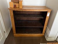 Straight-on view of the shelving unit showing two shelves and no doors, with seller's lot tag on the right side.