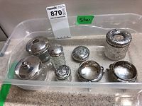 Seven sterling silver and glass vanity pots arranged in a plastic tray showing different lid designs and sizes.