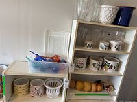 Full view of white shelving unit showing glass vases, planters, drinking glasses, and mushroom decor.