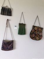 Four vintage ladies purses hanging on a wall, showing the variety in beadwork, mesh, and needlepoint material.
