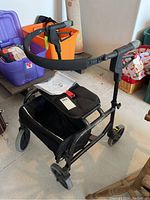 Full view of the black Nexus 3 mobility assist walker showing padded handles, curved safety bar, seat and storage basket under seat.