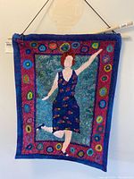 Full view of handmade wall hanging showing woman figure in blue dress with colorful circular border.