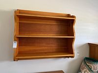 Full front view of wooden wall-mounted shelf showing two shelves and side curved detailing.