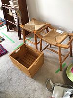 View of two wooden farmhouse stools with woven rush seats and wooden storage crate with handles placed on carpet.