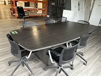 Conference table with 8 black office chairs around it, showing table surface and chair details.