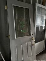 White exterior door with decorative leaded glass window and brass handle leaning against wall.