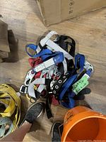 Photo of bundled fall arrest straps of various colors with metal hooks and labels on wooden floor.