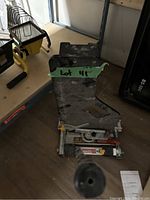 Full view of the floor cutting tool showing handle, base, and blade guard with lot number tag attached.