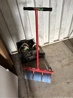 Full view of floor roller showing red T-handle and three blue carpeted rollers at base with some items behind it.