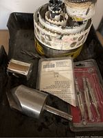 Set of metal hole saw blades with visible paint marks, stacked inside each other with various drill accessories around them.