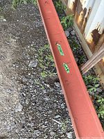 Full length view of red‐primer steel I-beam lying on gravel next to a corrugated metal container