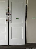 White 30-inch interior door shown standing against a wall with two rectangular panels, upper panel larger than lower panel.