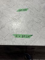 Close-up of the table top surface showing the marble-effect finish with a green tape label indicating Lot 150 and the table measurements 5 ft x 39.5 in x 29 in.