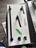 Photo of bathroom accessories mounted on display board, includes multiple towel bars, towel ring, and mounting hooks, black finish, branded Laloo, labeled Lot 8.