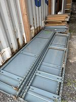 Photo of stacked gray metal racking shelving panels lying flat with some rust and wear visible.