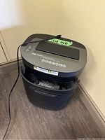 Full view of black and gray electric paper shredder with power cord, partially filled with shredded paper.