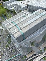 Photo showing bundled grey stone sills strapped on a wooden pallet outdoors, some grass and gravel visible.