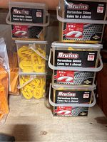 Multiple containers of Brutus Horseshoe Shims 3/16 inch (5 mm) packed in 100 count plastic boxes and plastic bags containing orange tile leveling wedges.