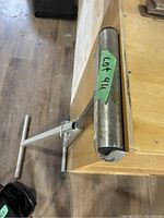 Photo showing metal wood holding tool clamped to the edge of a wooden workbench, featuring a horizontal round metal holding bar and supporting legs.