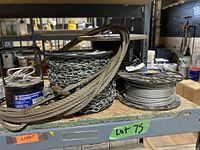 Photo of various metal cable and chain spools on a shelf, including thick steel cable, chain link spool, and thinner wire cable spool