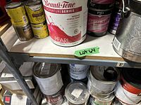 Multiple cans of paint on metal shelves including Beauti-Tone Signature Series Pearl White interior acrylic paint, Minwax wood finish stain, Para Premium velvet interior paint, and assorted others.