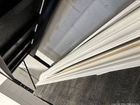 White various trim pieces stacked on black wood shelf against wall.