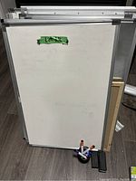 Full view of one wipe off board approximately 3 feet by 2 feet with aluminum frame, standing upright on the floor with a green tape label.