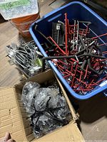 Plastic and metal wall hangers of various colors (red, black, silver) in boxes and containers, showing condition and types.