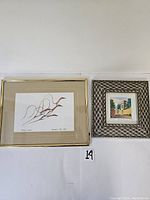 Photo of two framed artworks side by side on a white surface with measuring tape beside one frame