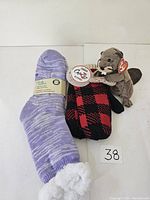 Photo shows a purple fuzzy sock, a pair of red and black plaid mitts, and a Canadian Beanie Beaver plush toy with tags.