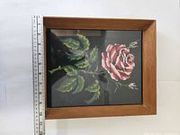 Framed cross stitched rose on black background with wooden frame, ruler placed for scale showing about 11 inches high.