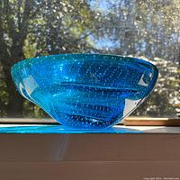 Side profile view of bright blue glass bowl with bubbles, showing thickness and translucence of glass in sunlight.