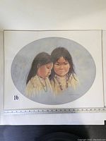 Photo shows the large oval-shaped print of two Indigenous girls, approximately 22 inches wide, with a measuring tape for scale. The print appears to be wrapped in plastic and mounted on cardboard.