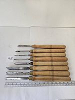 Top-down image of eight varying-sized wood handled metal chisels arranged in a row with a ruler for scale.