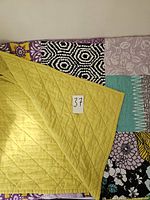 Top side and bottom side of the quilted bed cover showing multi-coloured patchwork design and yellow quilted backing with a lot number.